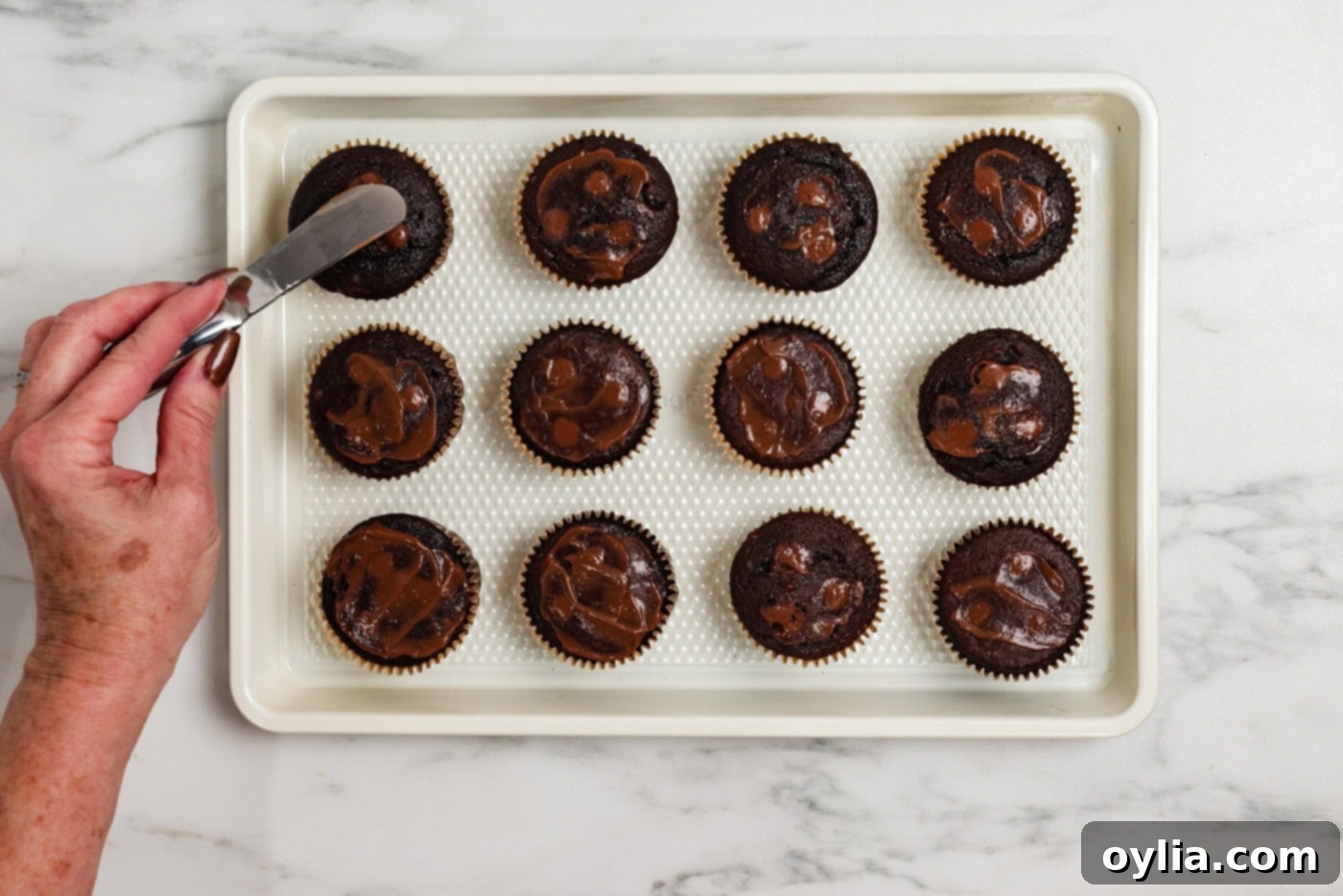 using a small spatula to smear chocolate pudding over the cupcake holes