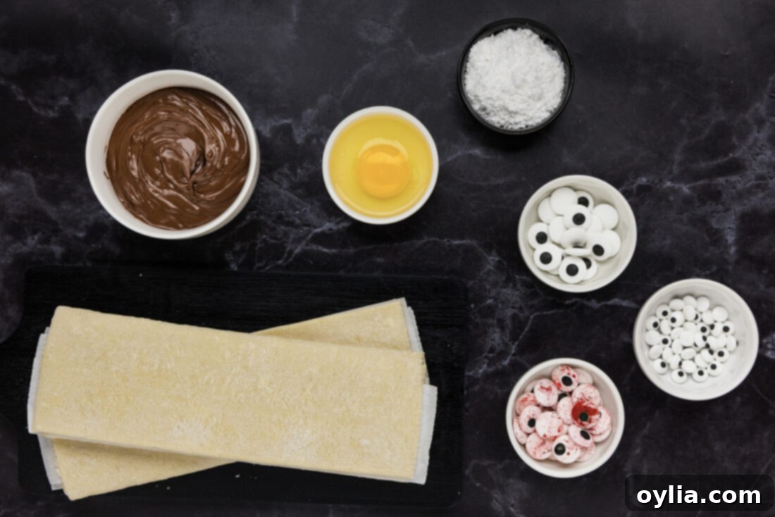 Bandaged Pastry Pockets 4 An organized display of ingredients for Mummy Hand Pies, including a box of puff pastry, jars of Nutella and jam, eggs, and candy eyeballs.