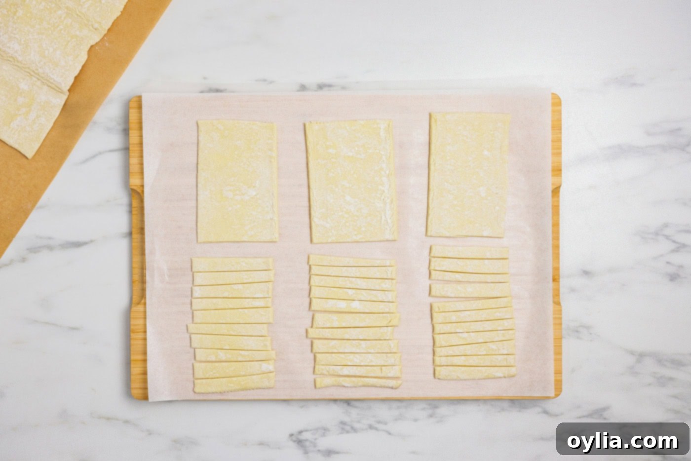 Bandaged Pastry Pockets 5 Puff pastry sheet divided into rectangular bases and thin strips for mummy bandages on a clean cutting board.