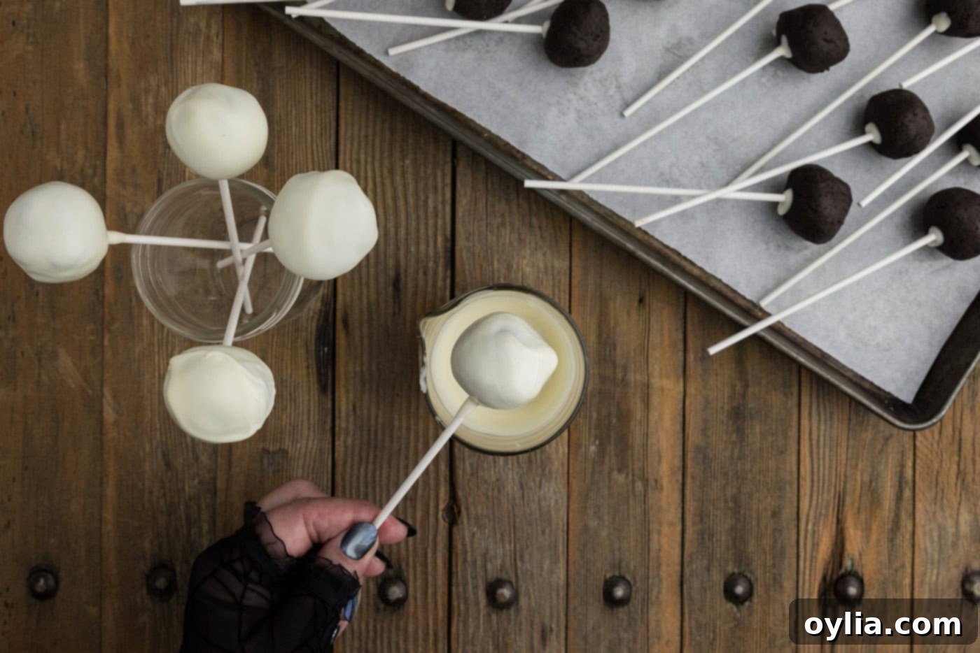 Hand dipping an Oreo truffle into a bowl of smooth white chocolate coating, holding onto the lollipop stick