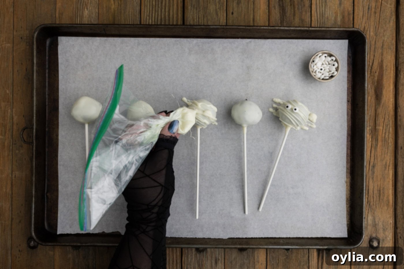 Drizzling melted white candy wafers over the top of white chocolate coated Oreo truffles to create mummy bandages, with candy eyes added