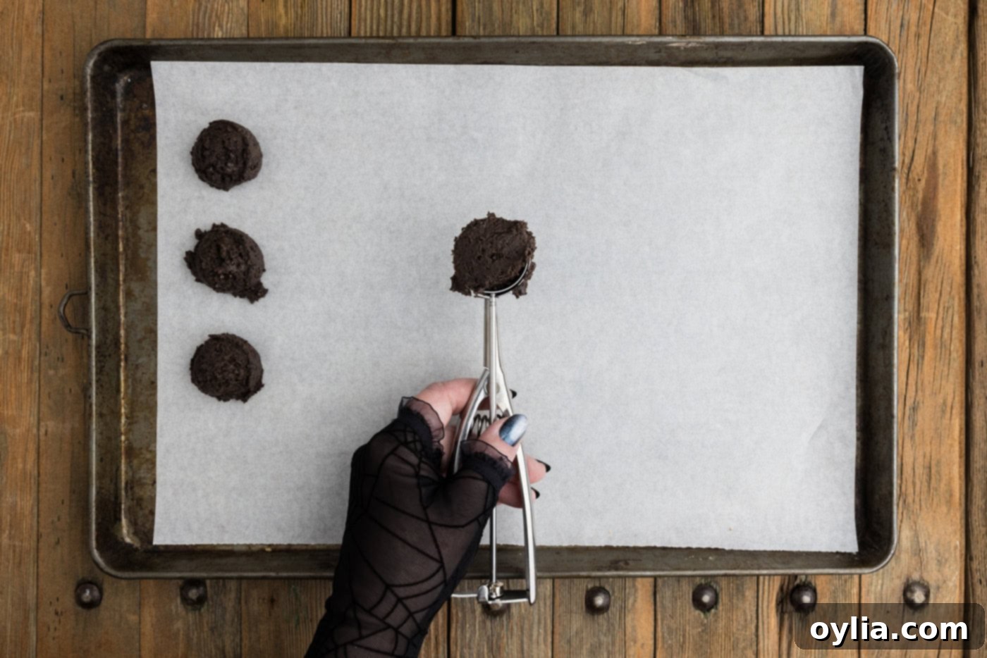 Tablespoon scoop of Oreo truffle mixture held over a parchment lined baking sheet, ready to be dropped