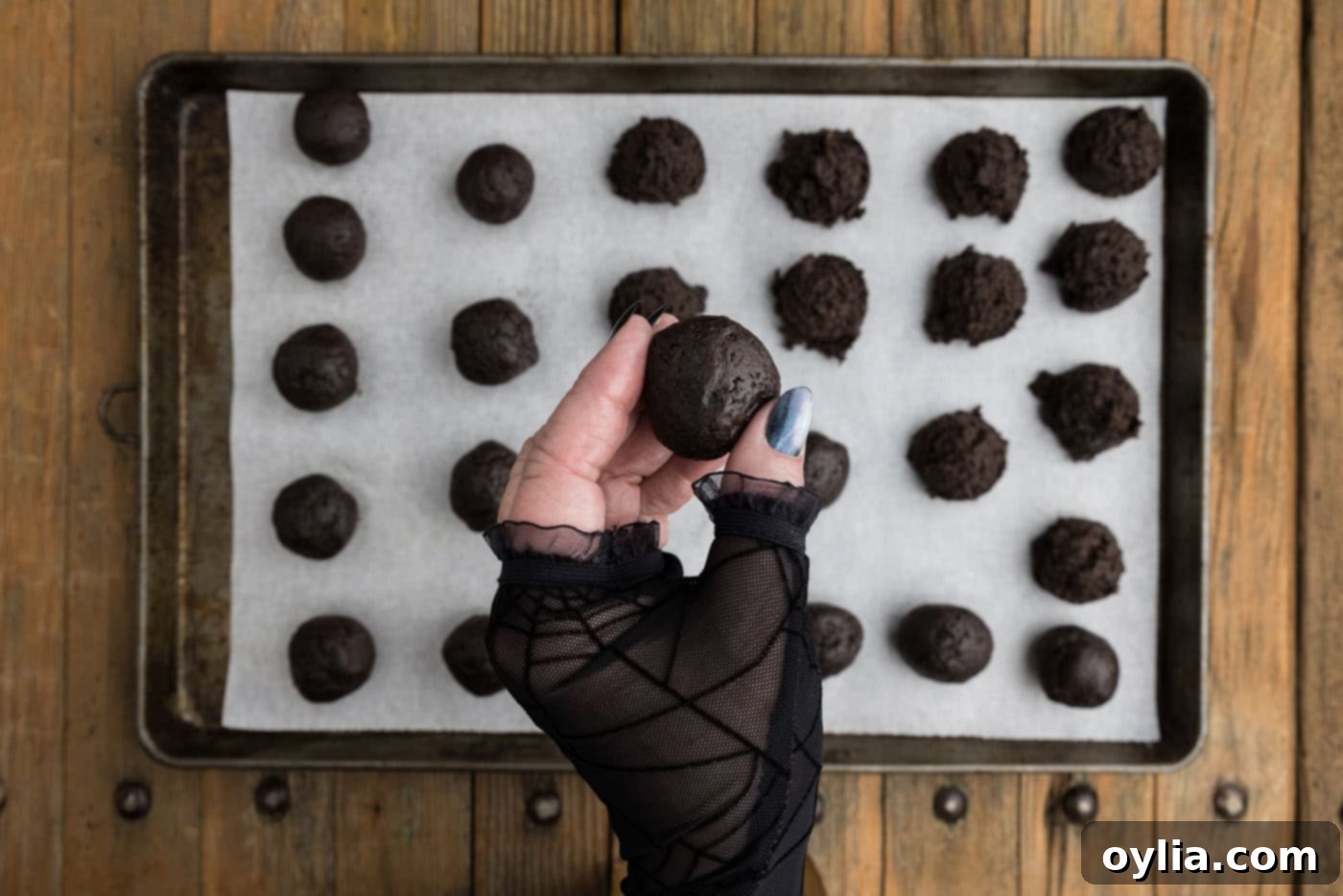 hand holding a perfectly rolled Oreo truffle ball over a baking sheet