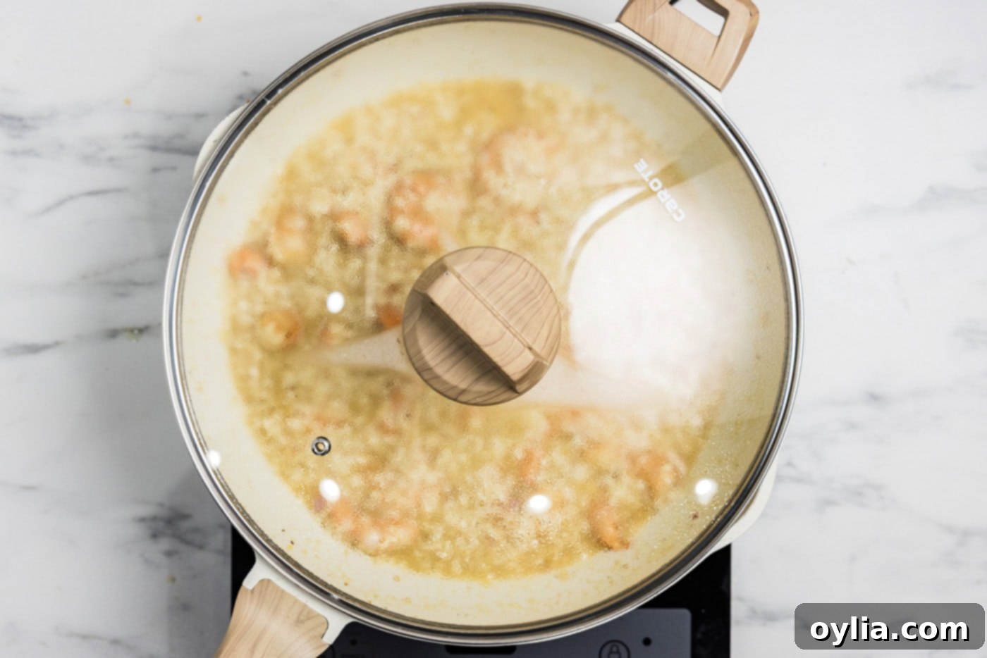 Shrimp risotto simmering in a skillet with a lid, finishing off the cooking process to meld flavors.