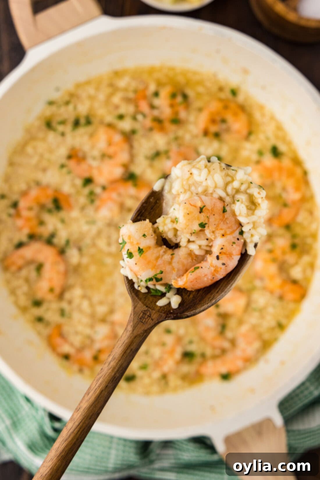 A spoonful of creamy shrimp risotto is held above a skillet filled with the finished dish, ready for serving.