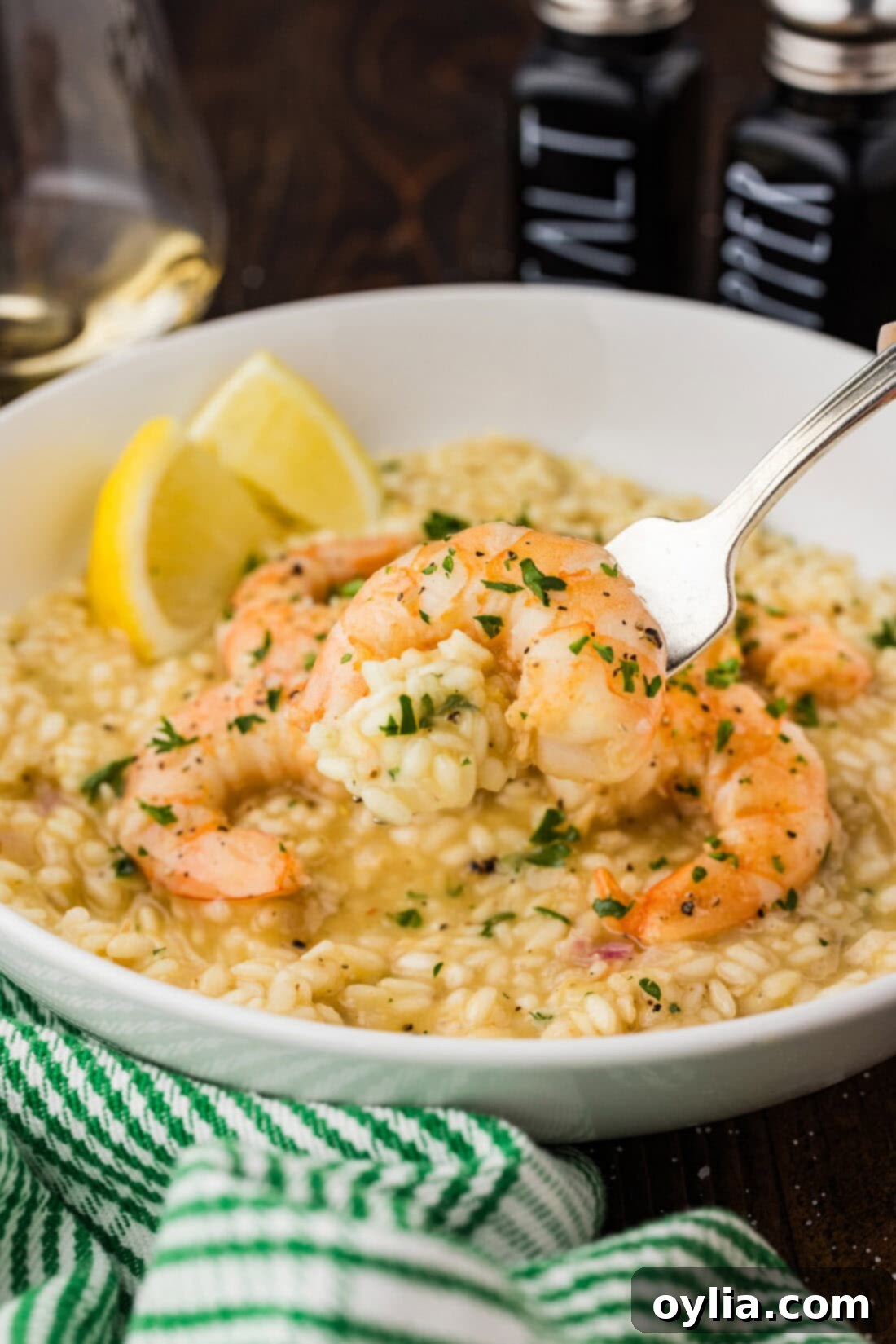 A fork lifts a generous serving of creamy shrimp risotto from a bowl, showcasing the perfectly cooked shrimp and the rich, velvety rice texture.