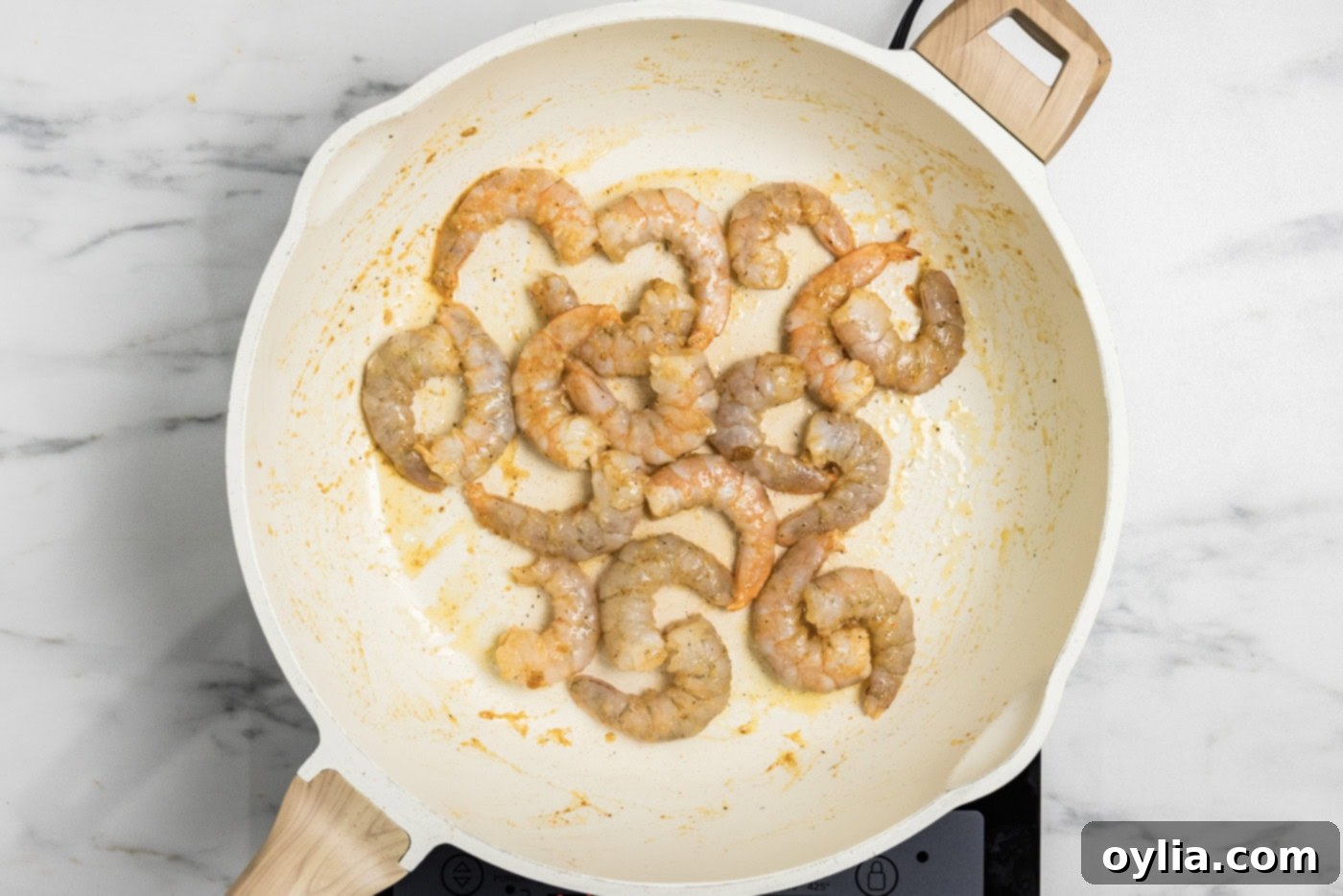 Partially cooked seasoned shrimp in a skillet, displaying a light pink color.