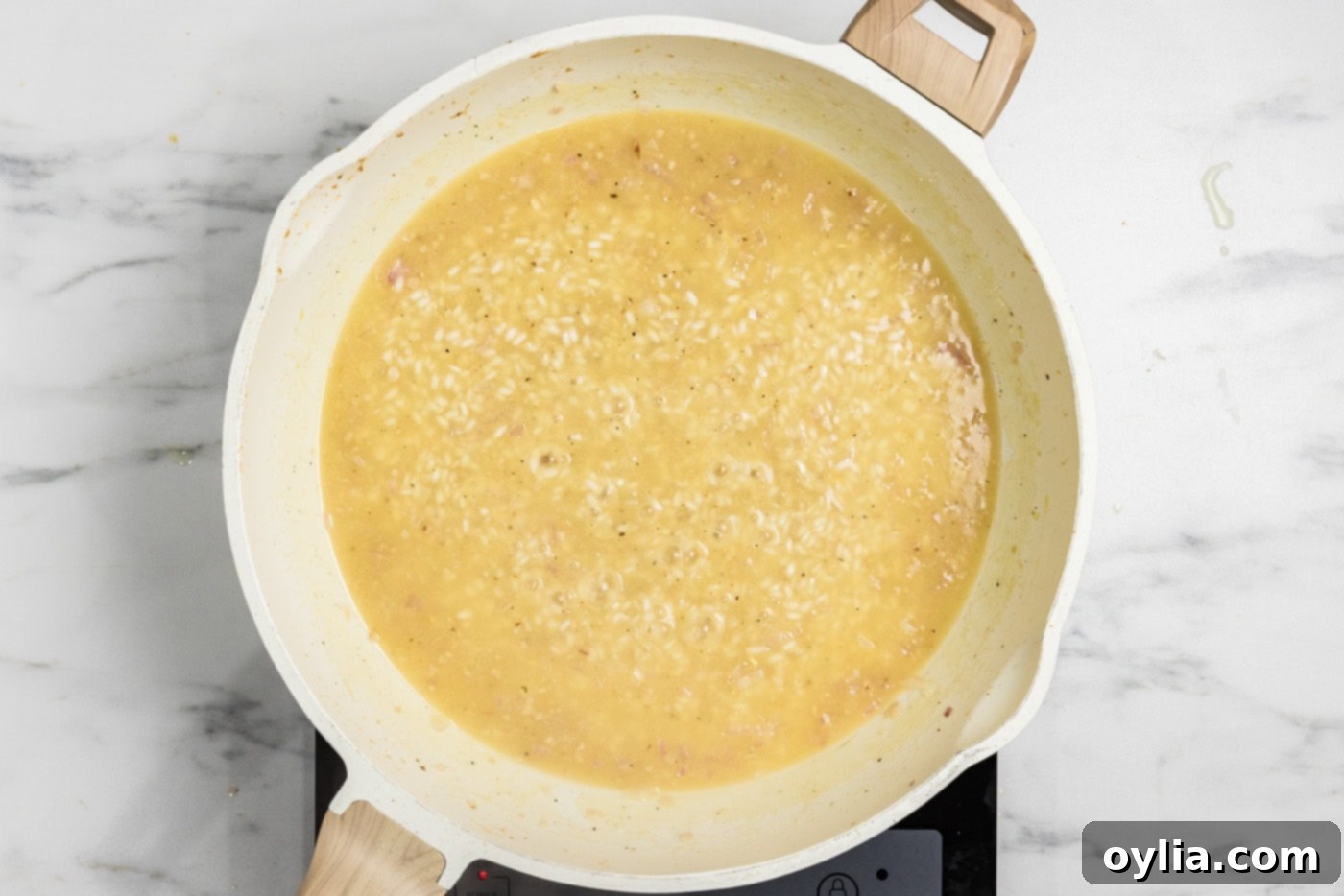 Chicken broth being added to the simmering risotto mixture in a skillet, illustrating the gradual addition process.