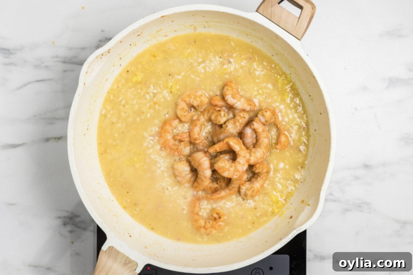 Partially cooked shrimp are added back into the creamy risotto mixture in the skillet, ready for final cooking.