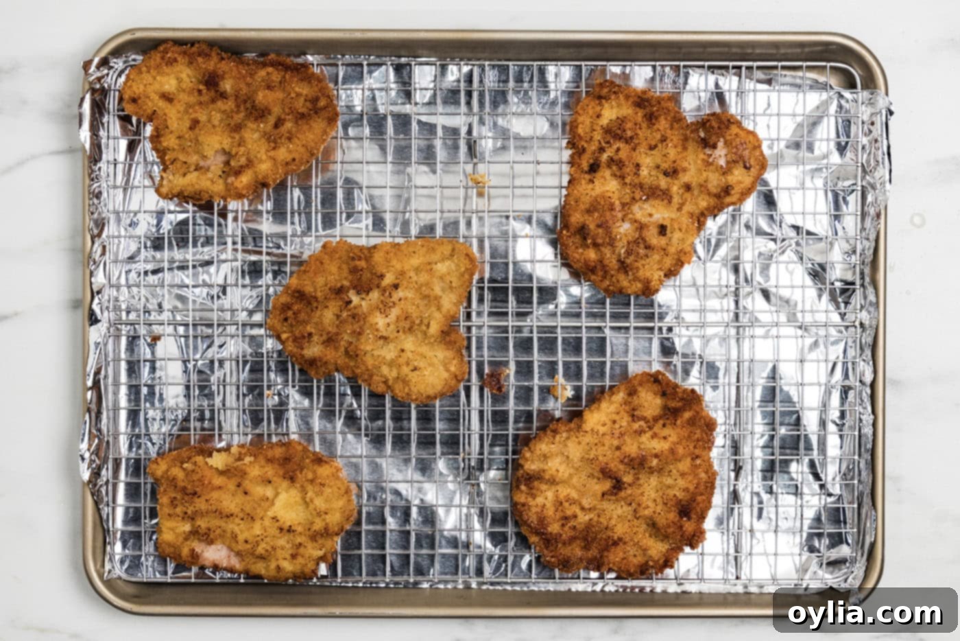 Cooked breaded veal cutlets on a wire rack over a baking sheet