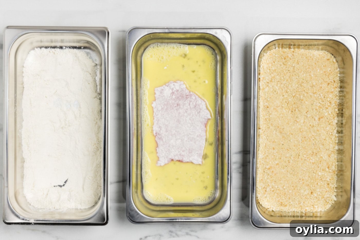 Floured veal cutlets in breading tray with egg