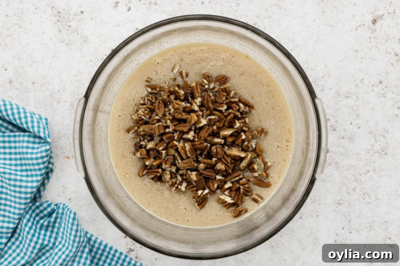 Chopped pecans being added to the pecan pie filling in a mixing bowl, ready to be folded in.