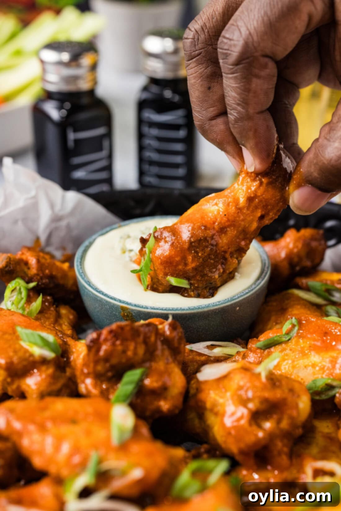 A close-up of a crispy Buffalo Chicken Wing being dipped into a bowl of creamy blue cheese dressing.