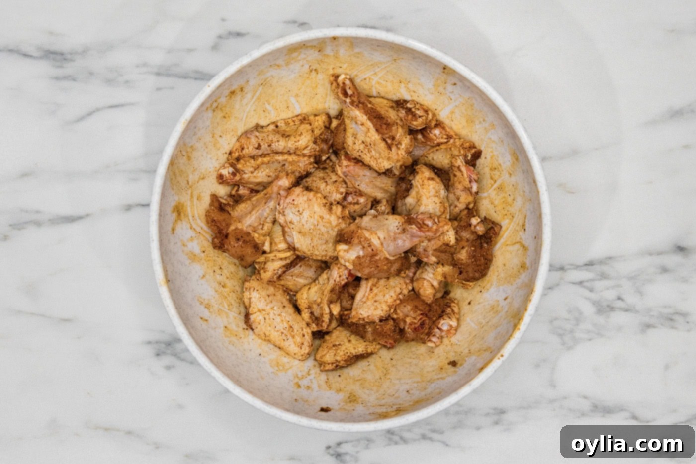 Chicken wings in a large mixing bowl, thoroughly tossed and covered in a flavorful wet rub.