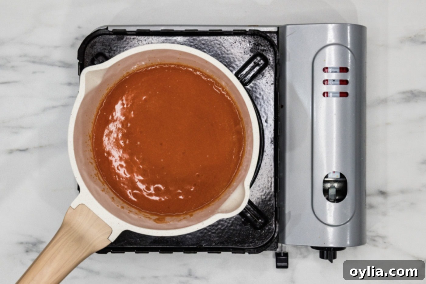 Homemade buffalo sauce simmering gently in a medium saucepan on the stovetop.
