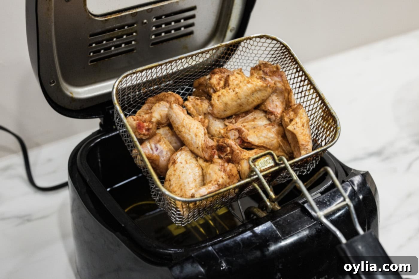 A fryer basket filled with seasoned chicken wings being slowly lowered into a deep fryer containing hot oil.