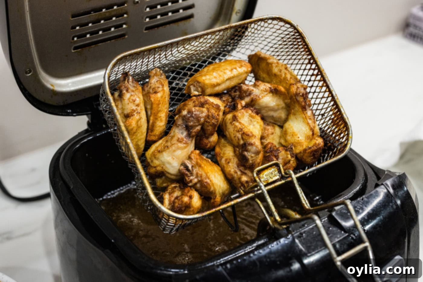 A fryer basket being lifted out of a deep fryer, revealing golden-brown, crispy chicken wings.