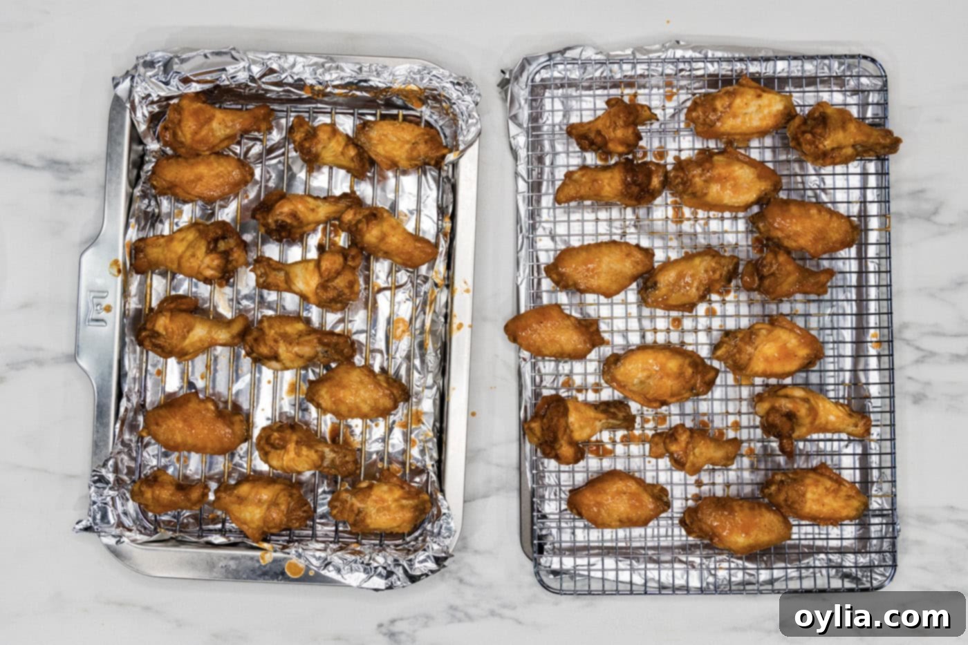 Sauced chicken wings neatly arranged in a single layer on a wire rack set over a baking sheet, ready for the oven.