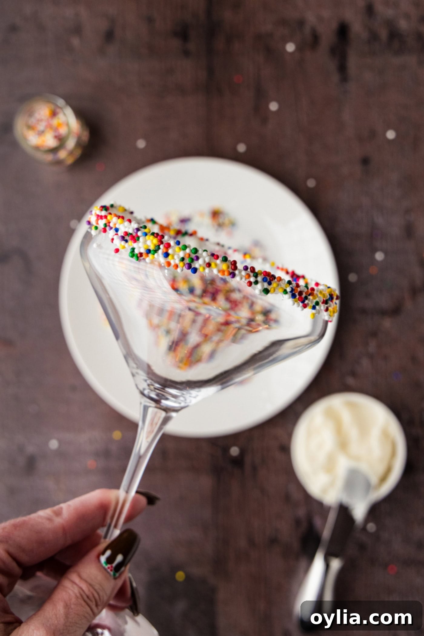 holding a martini glass with the rim coated in frosting and rolled in sprinkles