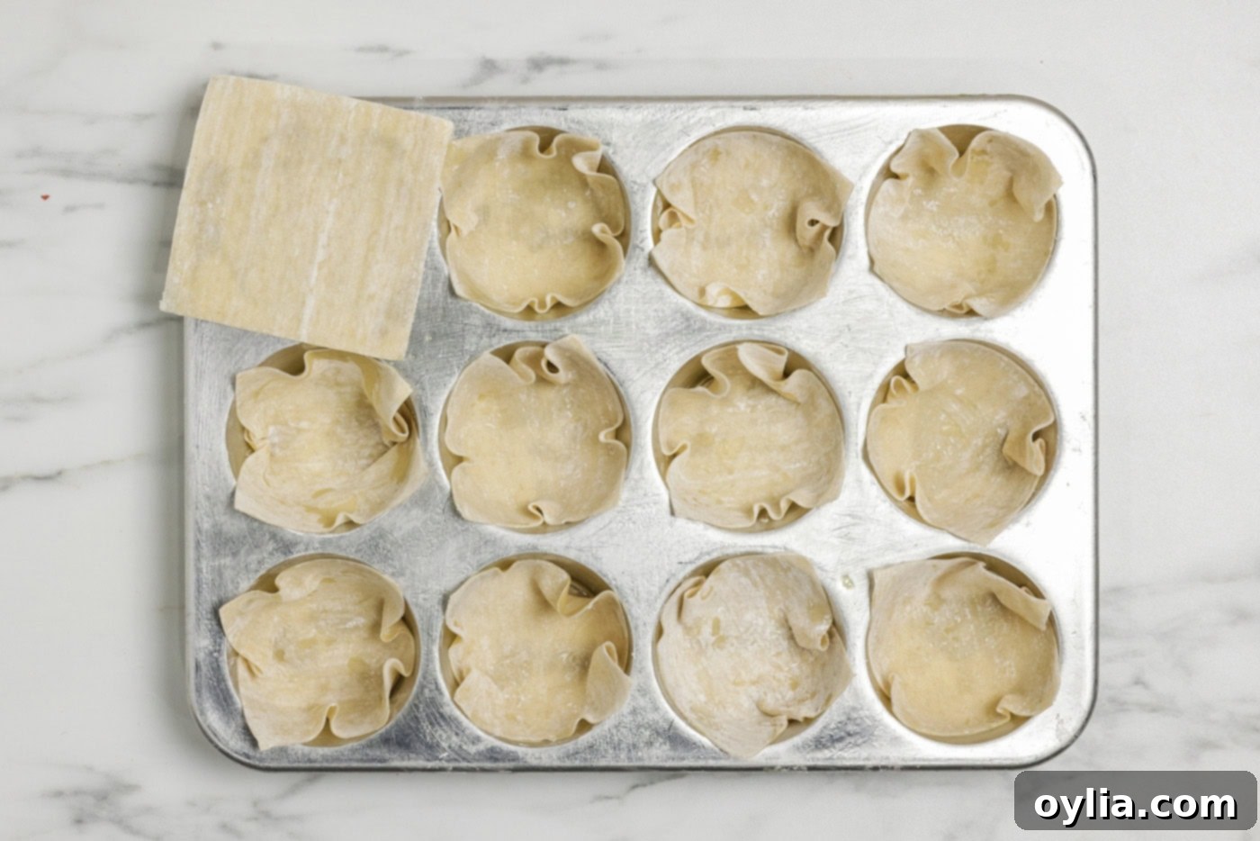Wonton wrappers tucked inside muffin pan cavities