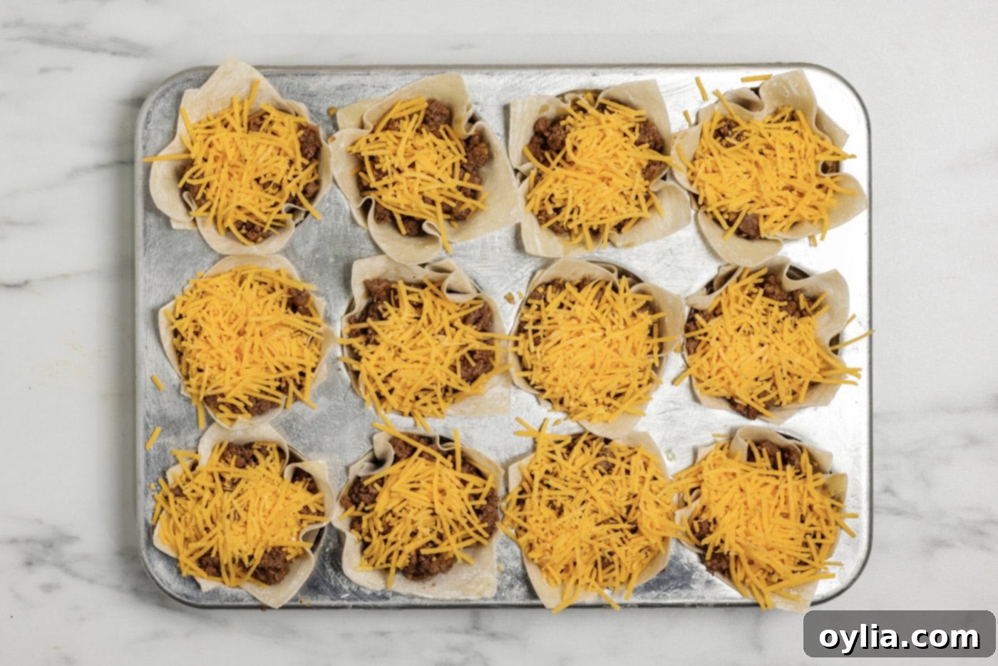 final layer of shredded cheese on top of taco cups in a muffin pan