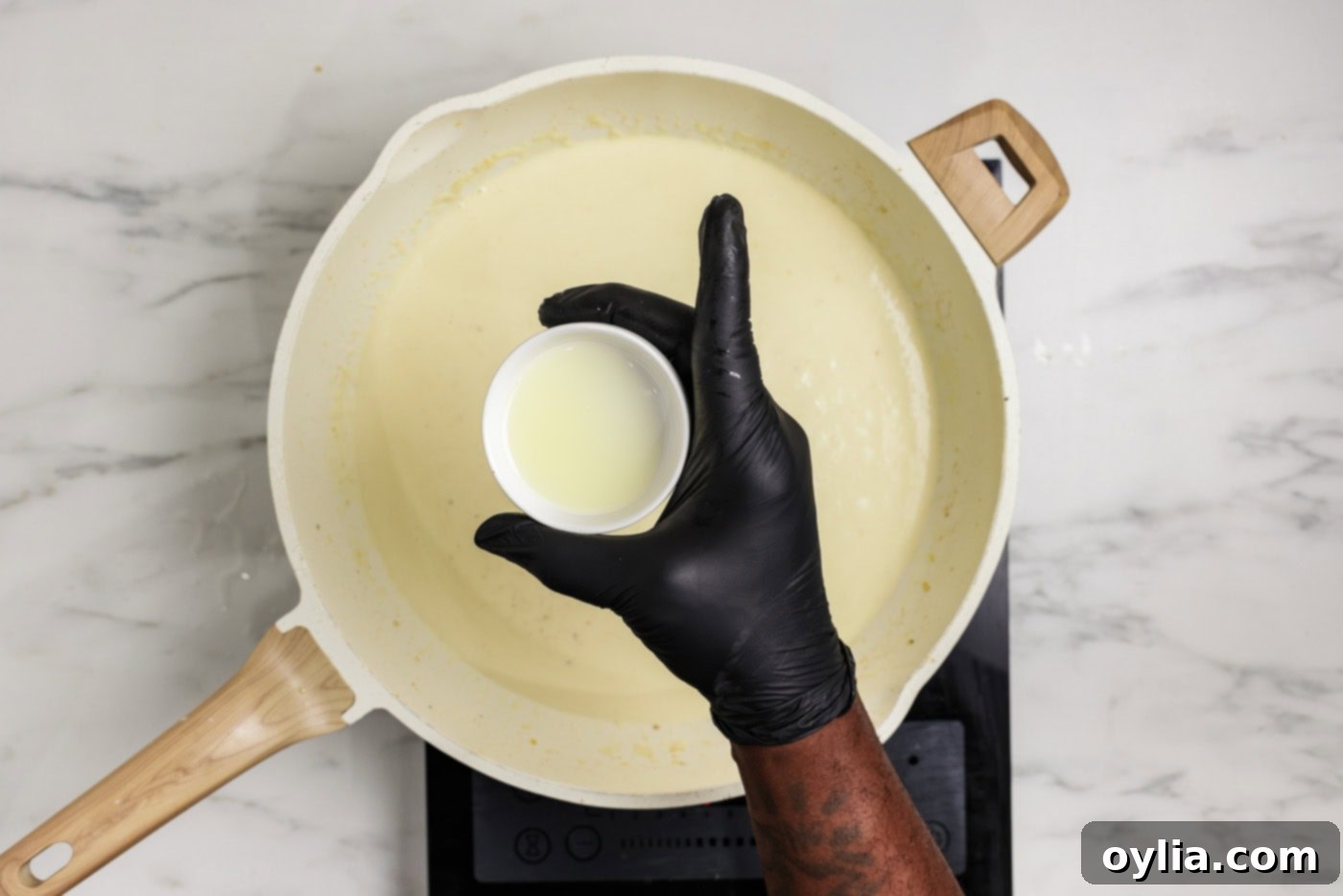 hand holding a small bowl of lemon juice over a skillet of garlic cream sauce