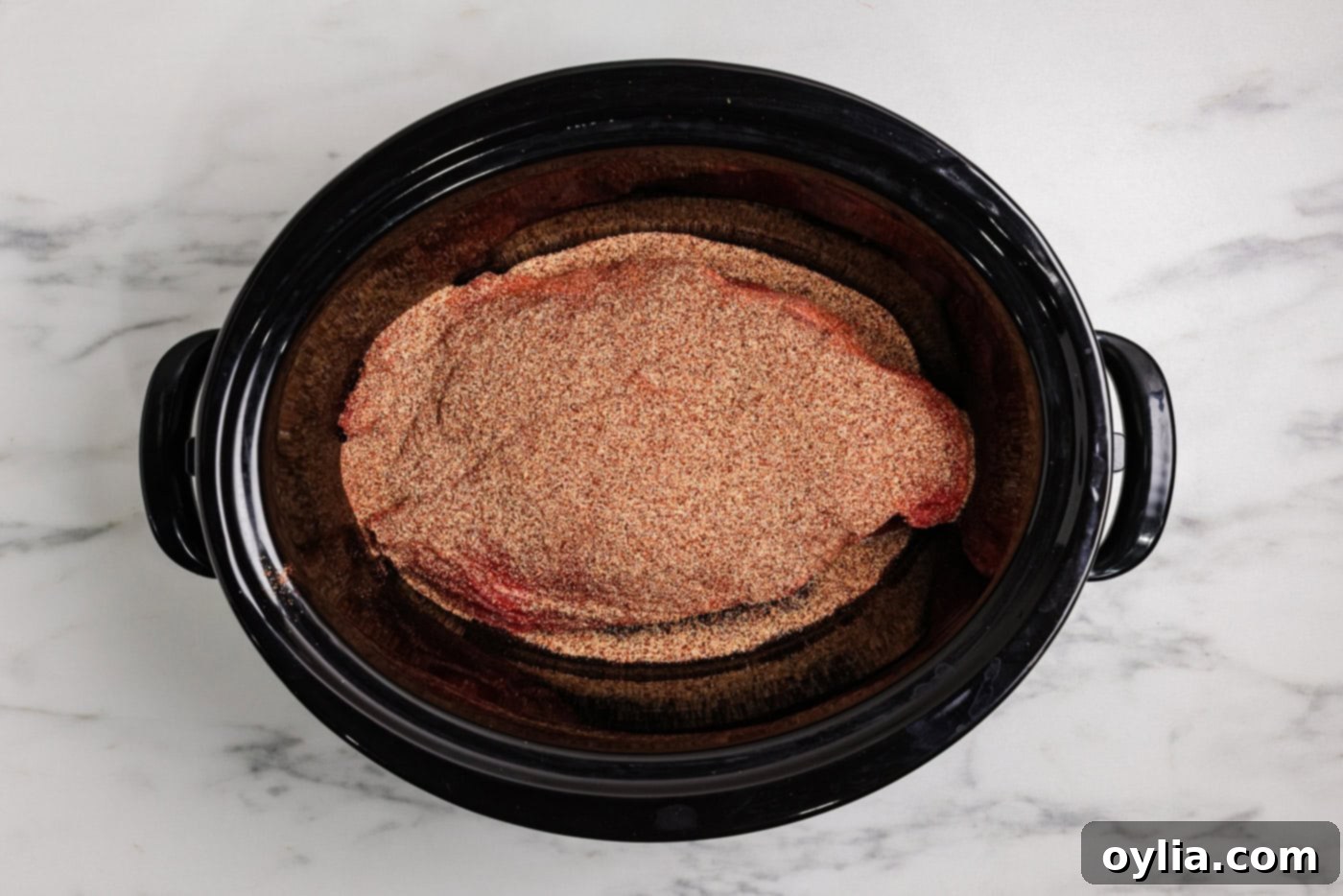 chuck roast in a slow cooker covered with seasonings