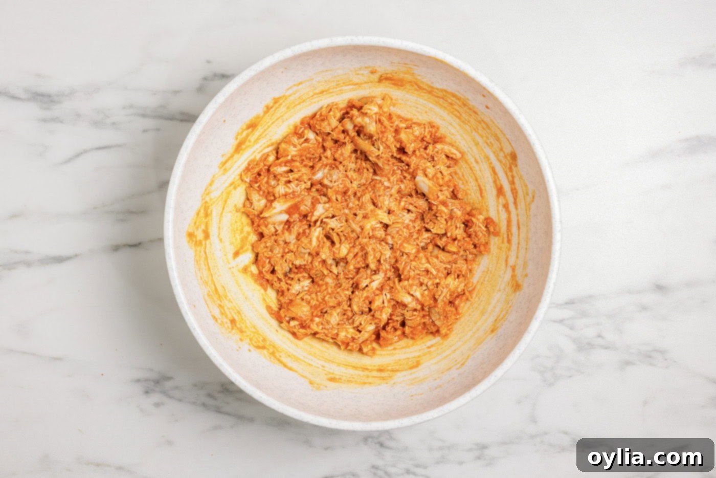 Shredded chicken in a bowl mixed with buffalo sauce