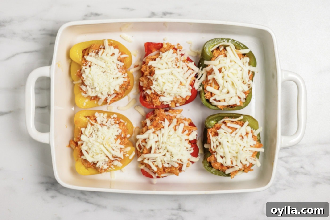 Mozzarella cheese on top of buffalo chicken stuffed peppers in a baking dish