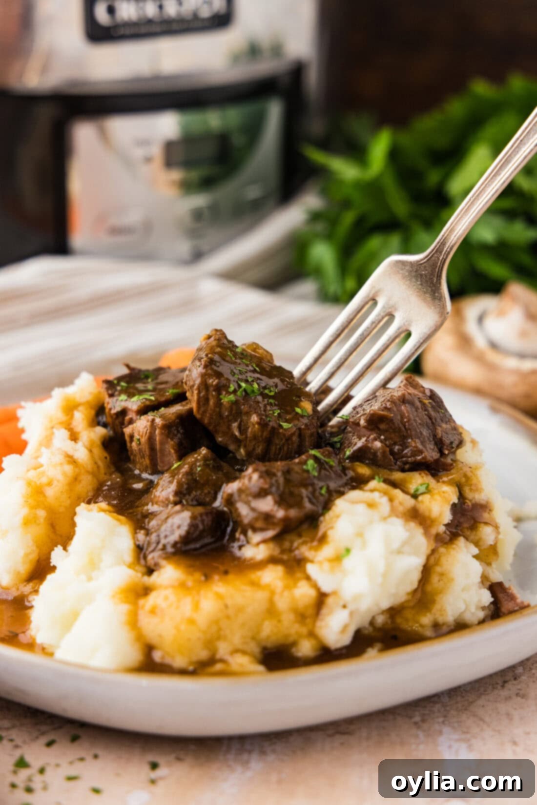 Fork pressing into Crockpot Beef Tips and Gravy served over mashed potatoes
