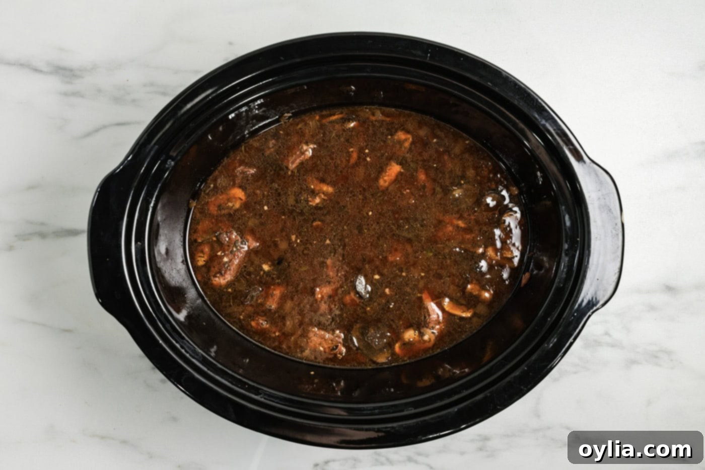 Beef broth added to crock pot with cubed beef, mushrooms, onions, and seasonings